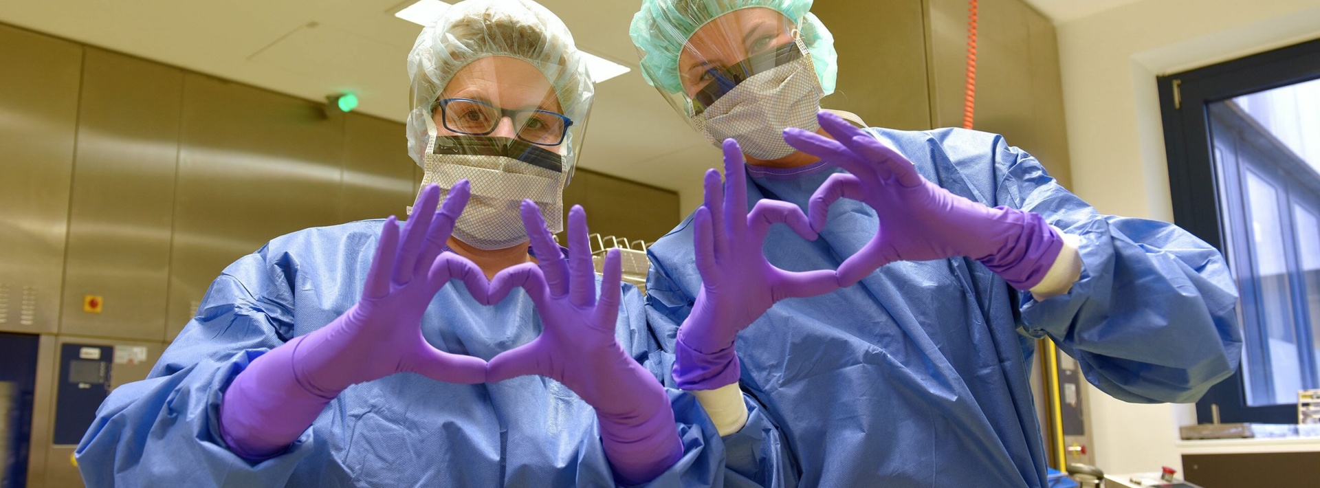 Medizinische Angestellte in Schutz-Aussrüstung bilden ein Herz mit ihren Händen